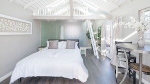 Ein Schlafzimmer mit einem großen Bett, einem Schreibtisch und einem Stuhl. Eine Treppe führt zu einer oberen Ebene.
