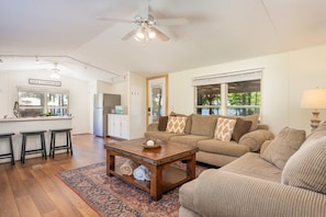 A spacious living area with a kitchen, a dining area with stools, a sofa set, and a ceiling fan.