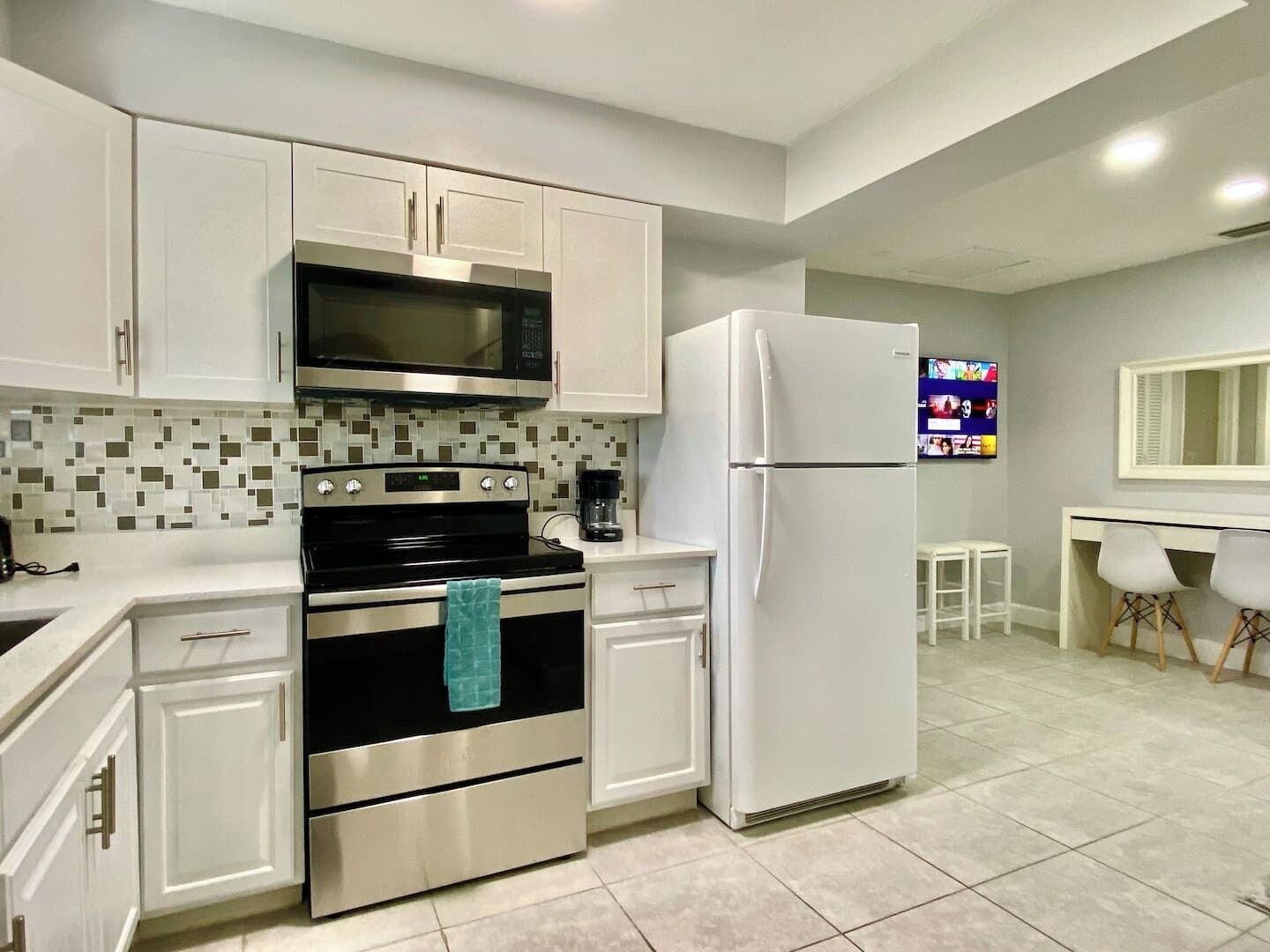 A modern kitchen with white cabinets, a stainless steel oven, a microwave, and a white refrigerator.