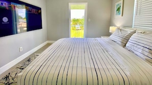 Ein Schlafzimmer mit einem großen Bett, einem an der Wand befestigten Fernseher und Blick ins Freie durch eine Tür.