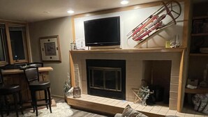 A living room with a fireplace, a television mounted above it, and a ski rack on the wall.