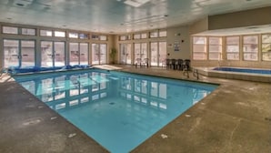 An indoor swimming pool with clear glass walls, a tiled floor, and several chairs around the pool.