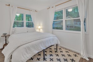Une chambre à coucher avec un lit, une table de chevet, une lampe et une fenêtre avec des rideaux.