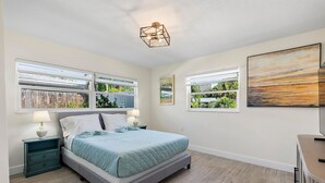 Un dormitorio con cama, mesitas de noche, un cuadro y ventanas con vistas.