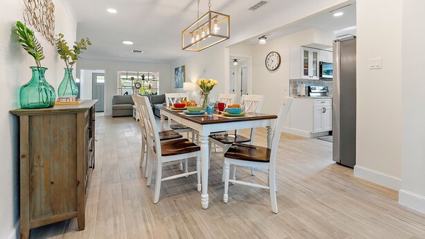 Una cocina moderna con armarios blancos, un comedor con mesa y sillas de madera, y un elemento decorativo en la pared.