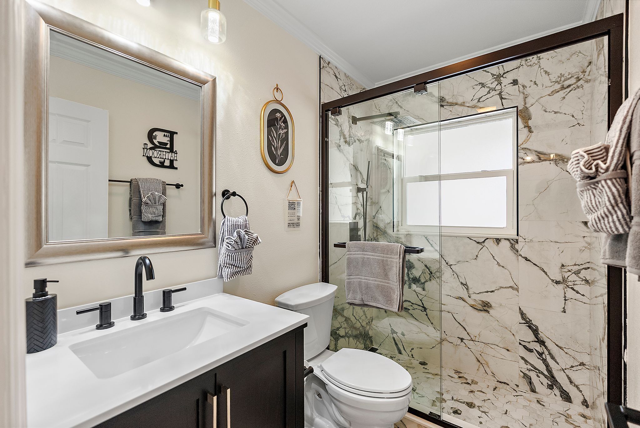 A modern bathroom with a white sink, black faucets, a toilet, and a glass shower enclosure.