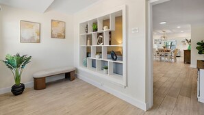 Un interior moderno con un banco, un estante blanco con adornos y un área de comedor al fondo.