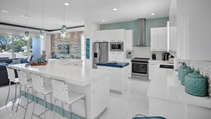 Una cucina moderna con mobili bianchi, un'isola centrale, elettrodomestici in acciaio inossidabile e vista sull'esterno.