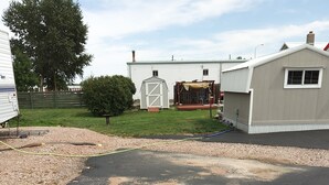 Una propiedad residencial con entrada pavimentada, un cobertizo pequeño, zona de estar al aire libre techada y un árbol grande.