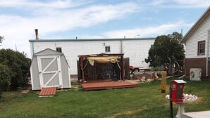 Un patio trasero con terraza de madera, un cobertizo y una zona de estar techada.