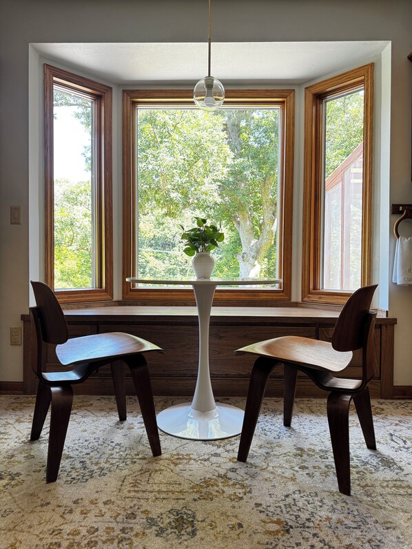 A corner room with a bay window, two chairs, a small table, and a hanging light fixture. - River Retreat in Mid-Modern Home in Park Setting (Iowa Falls)