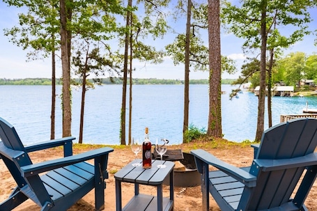 A lakeside view with two Adirondack chairs, a small table, and a bottle of wine.. Cozy Cedar Waterfront Cabin 10 on Toledo Bend