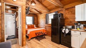 Una habitación tipo cabaña, compacta, con cama, refrigerador, estufa y una pequeña kitchenette.