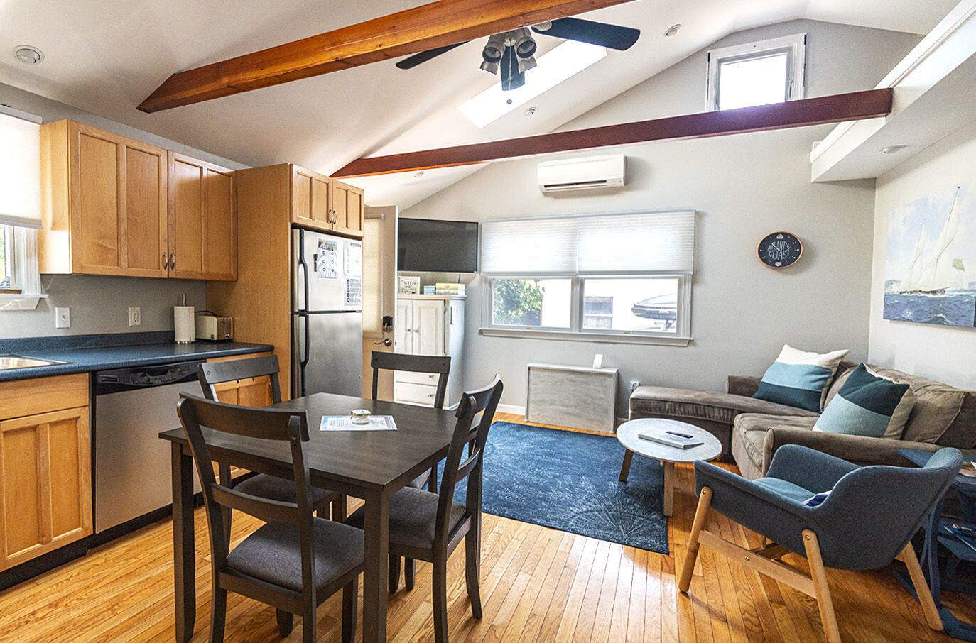 A compact kitchen with wooden cabinets, a dining table, and chairs. There is a small seating area with a sofa and a coffee table.