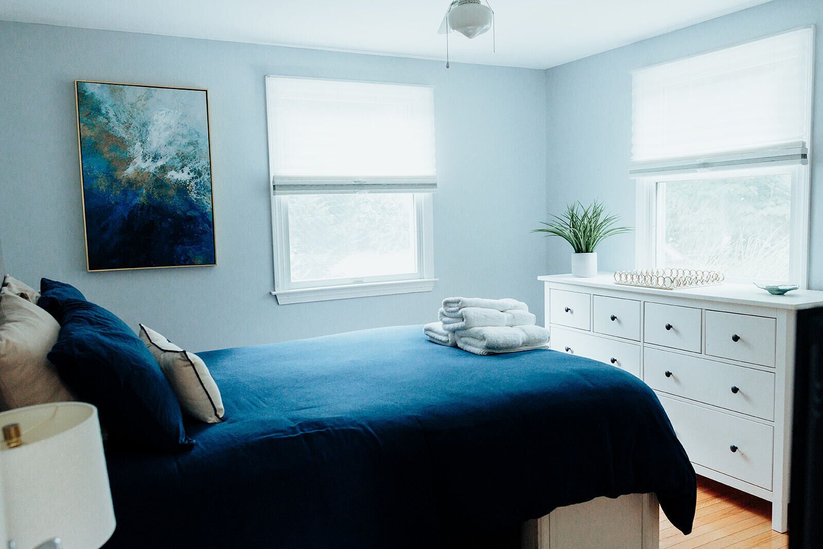 Une chambre à coucher avec un lit, une commode, une plante en pot et un tableau.