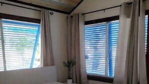 A bedroom with a large bed, two windows with curtains, a bedside table with a plant, and a wooden ceiling. - Cozy & Private Home at US Coral Reef Capital (Key Largo)