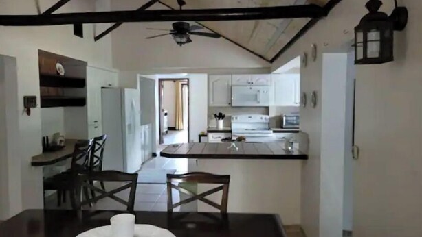 A modern kitchen with white cabinets, a central island, and a dining area with a dark table and chairs. - Cozy & Private Home at US Coral Reef Capital (Key Largo)