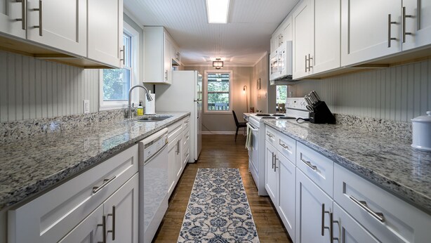 Una cocina moderna con armarios blancos, encimeras de granito y una alfombra estampada.