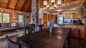 A wooden interior with a dining table, chairs, a sofa, and a kitchen area with appliances.