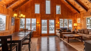 A spacious wooden cabin with a high ceiling, large windows, a dining area, and a cozy living room.