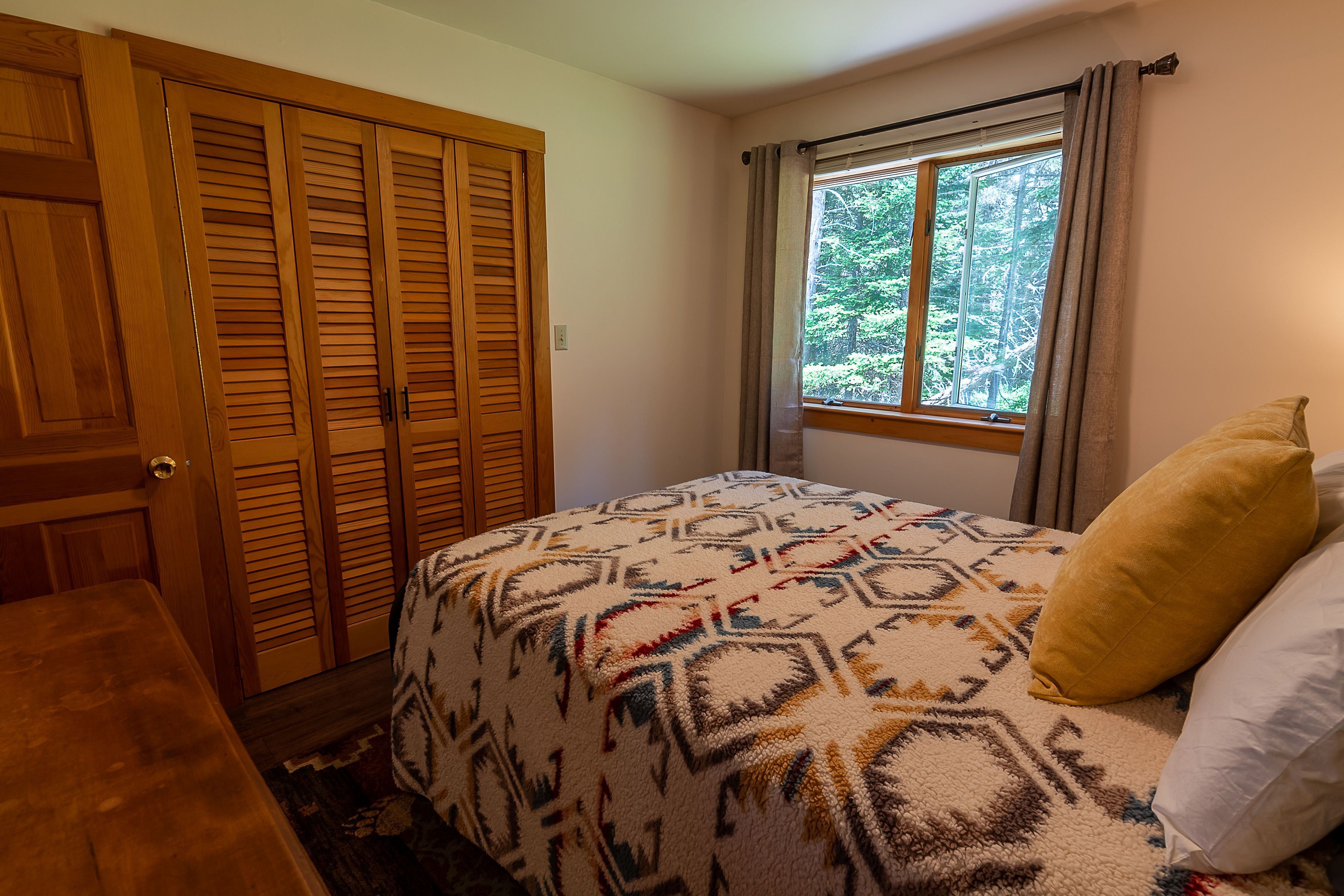 A bedroom with a bed, a window with curtains, and a wooden wardrobe.