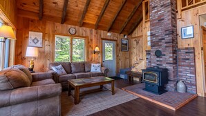 A cozy wooden cabin interior with a fireplace, two sofas, a coffee table, and framed pictures on the walls.