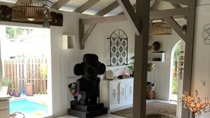 A spacious living area with a high ceiling, a wooden table with decorative items, a statue, and a view of a swimming pool outside. - PROMO: CHARMING POOL VILLA LES TROIS ILETS 3 bedrooms sleeps 8. WATCH  (Les trois ilets)