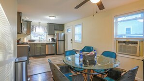 A compact kitchen with modern appliances, a dining area with a glass table and blue chairs, and a ceiling fan. - Guest Fave Cape-Cod Style Retreat with Main-Level Bedroom bordering Farmington (New Britain)
