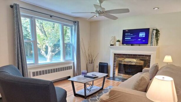 A living room with a fireplace, a television, and a ceiling fan. - Guest Fave Cape-Cod Style Retreat with Main-Level Bedroom bordering Farmington (New Britain)