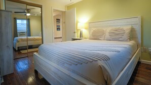 A bedroom with a large bed, a ceiling fan, a nightstand with a lamp, and a mirror. - Guest Fave Cape-Cod Style Retreat with Main-Level Bedroom bordering Farmington (New Britain)