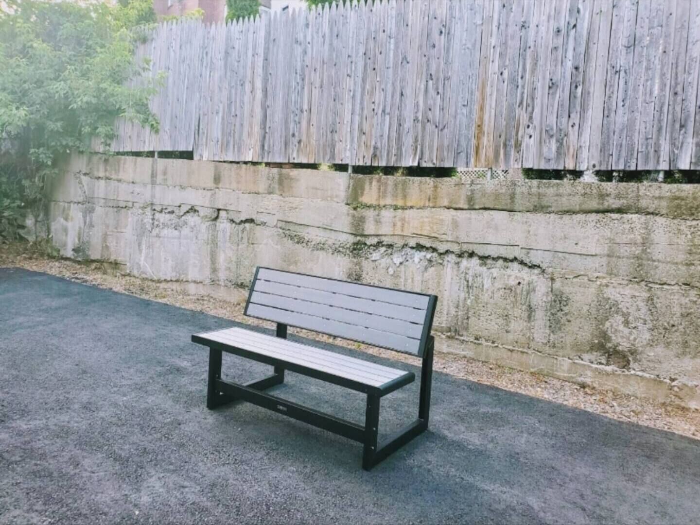 Een bank tegen een betonnen muur, met een houten hek op de achtergrond.
