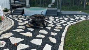 Un espace patio aménagé avec un revêtement de sol en pierre et gravier, un foyer extérieur, du mobilier de jardin et un coin salon abrité.