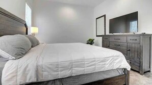 Une chambre à coucher avec un lit, une commode, une télévision et une petite plante.
