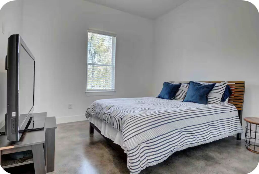 Un dormitorio con una cama, un televisor sobre un mueble bajo y una ventana con persianas.
