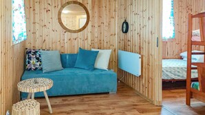 Una habitación acogedora con un sofá azul, un espejo redondo, suelo de madera y una cama con cabecera blanca.