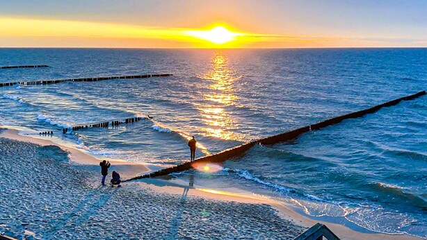 Una playa con atardecer, olas y un muelle.