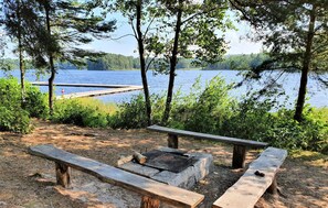 Ein Campingplatz am Seeufer mit Picknicktischen und Feuerstelle.
