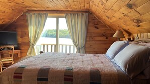 Un dormitorio acogedor con una cama grande, paredes de madera, una ventana con cortinas, una silla y una lámpara.