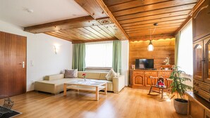A cozy living room with a sofa, coffee table, and a television in a wooden cabin-style room. - gemuetliche Ferienwohnung (Dalaas)