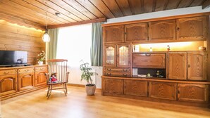 A cozy living room with wooden flooring, a television, a rocking chair, and a large wooden cabinet with glass doors. - gemuetliche Ferienwohnung (Dalaas)