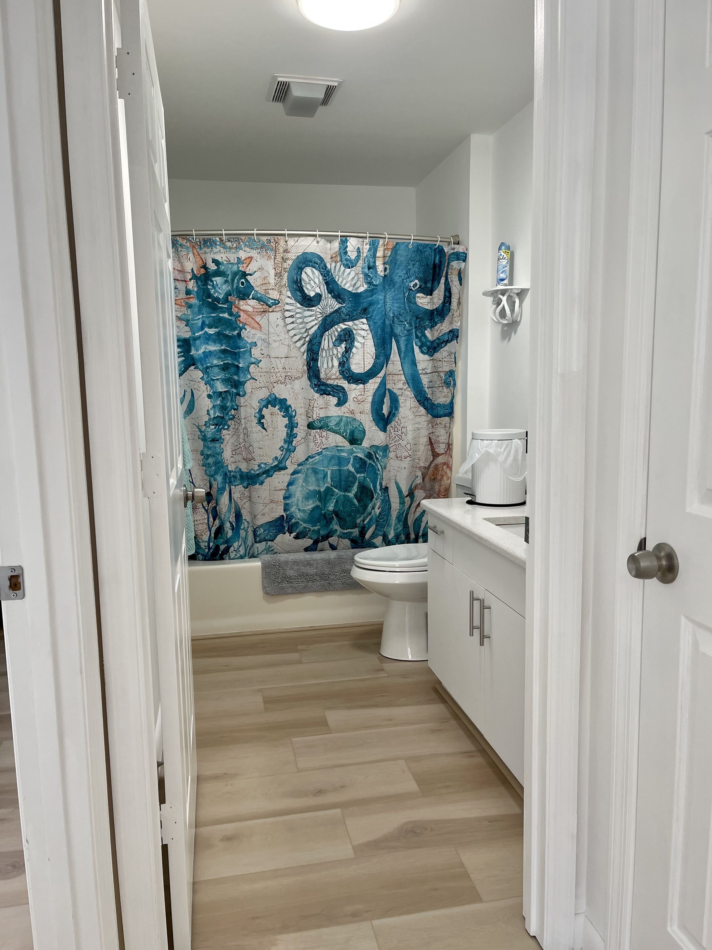 Ein Badezimmer mit einer Duschvorhang, der ein blaues Oktopus-Muster zeigt, einer weißen Toilette und einem Waschbecken mit Seifenspender.