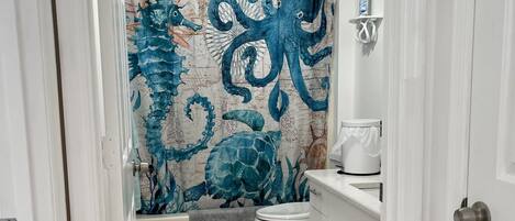 Ein Badezimmer mit einer Duschvorhang, der ein blaues Oktopus-Muster zeigt, einer weißen Toilette und einem Waschbecken mit Seifenspender.