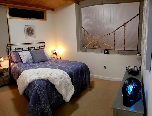 Une chambre avec un lit, un hamac fixé au mur, une horloge murale et un ventilateur.