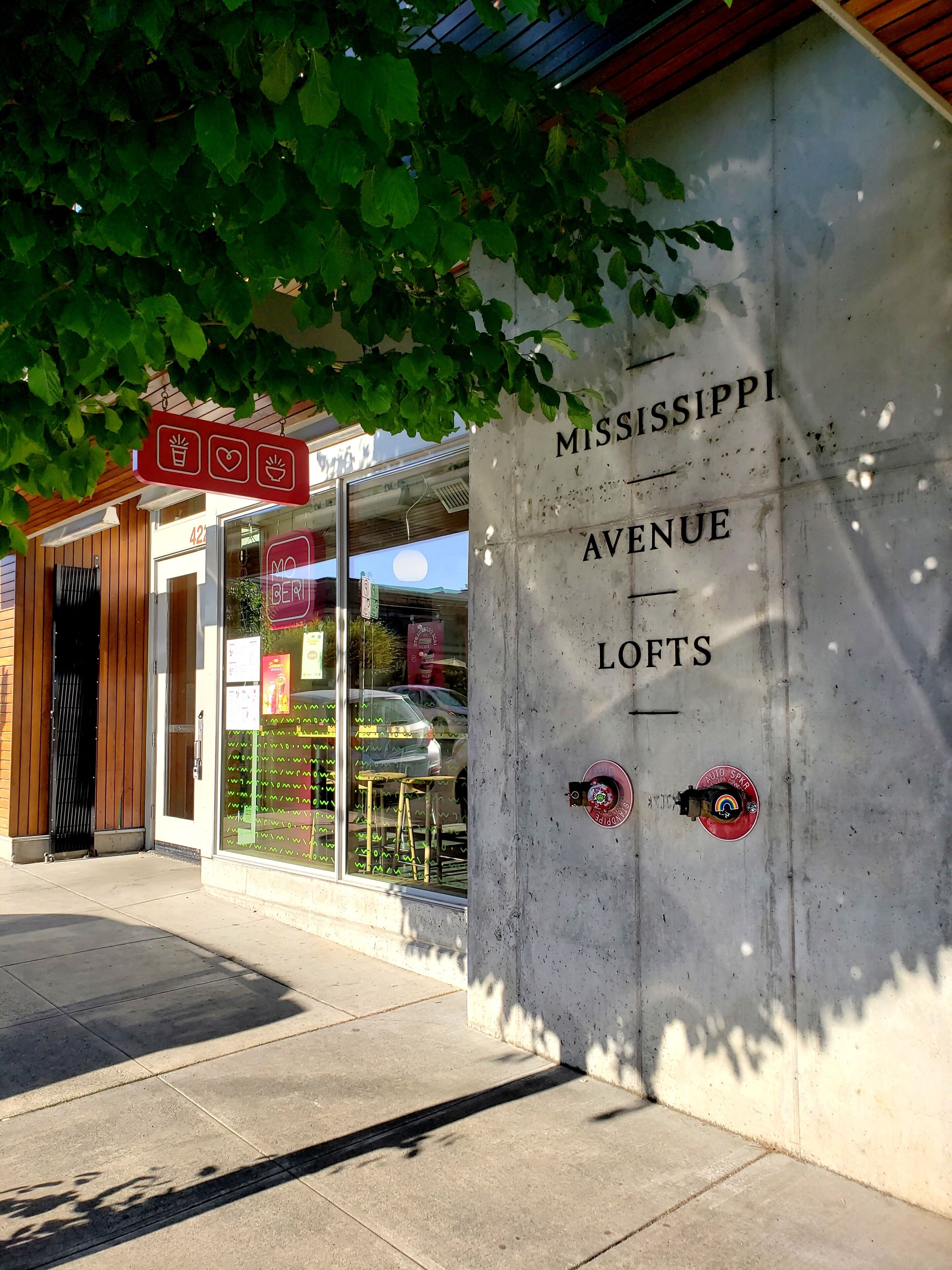 A building with a sign reading "Mississippi Avenue Lofts" and a storefront with a neon sign.