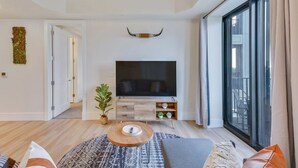 Un salon moderne avec un téléviseur à écran plat, une table basse et une grande fenêtre.