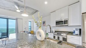 Une cuisine moderne dotée d’un grand îlot en granit, d’appareils électroménagers en acier inoxydable et offrant une vue sur l’extérieur.
