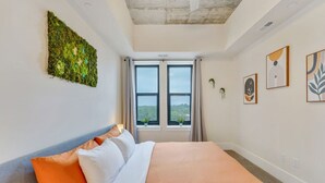 Une chambre d’hôtel moderne, dotée d’un grand lit, offrant une vue sur l’extérieur par une fenêtre et agrémentée d’œuvres d’art sur les murs.