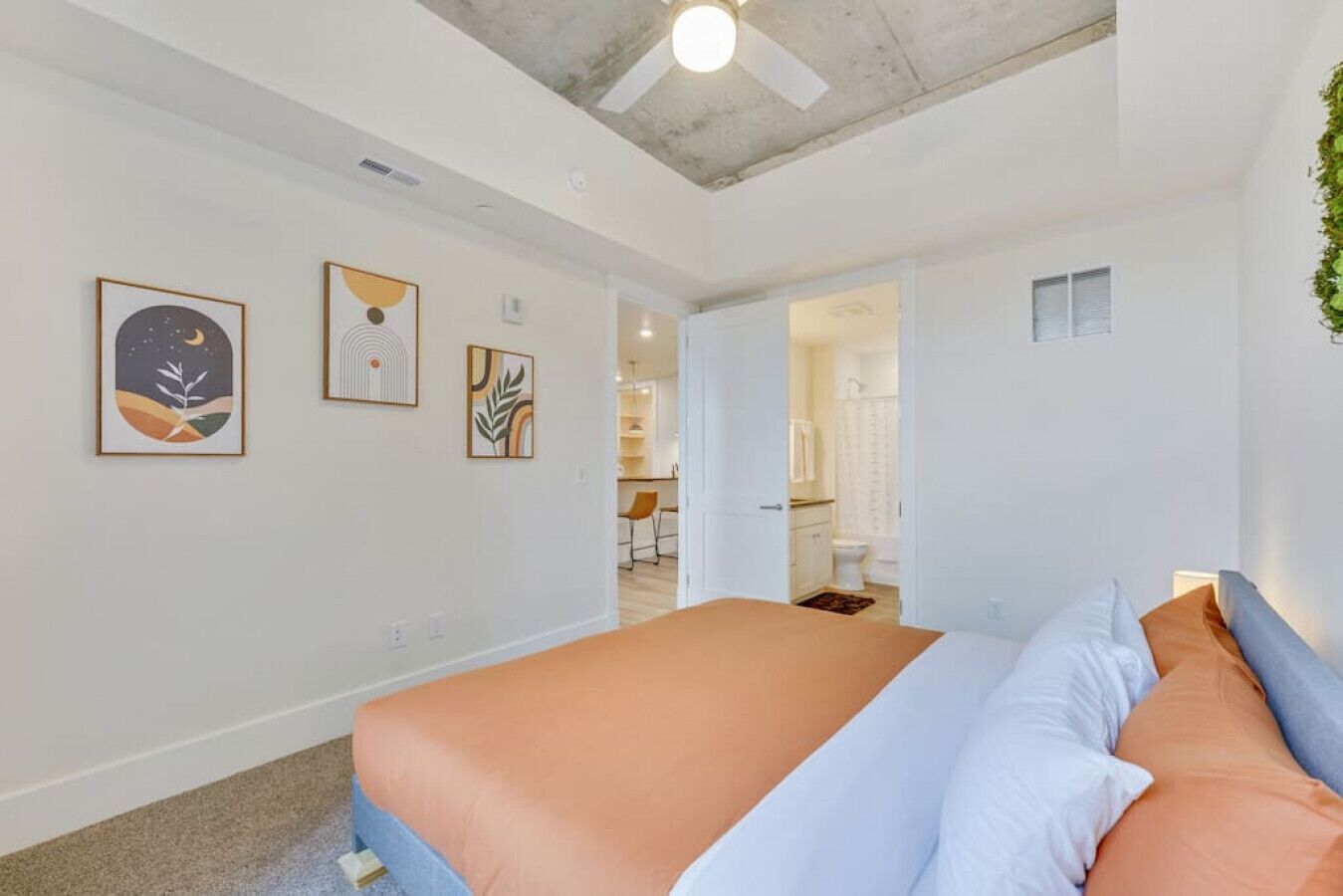A modern bedroom with a large bed, a ceiling fan, and artwork on the walls.