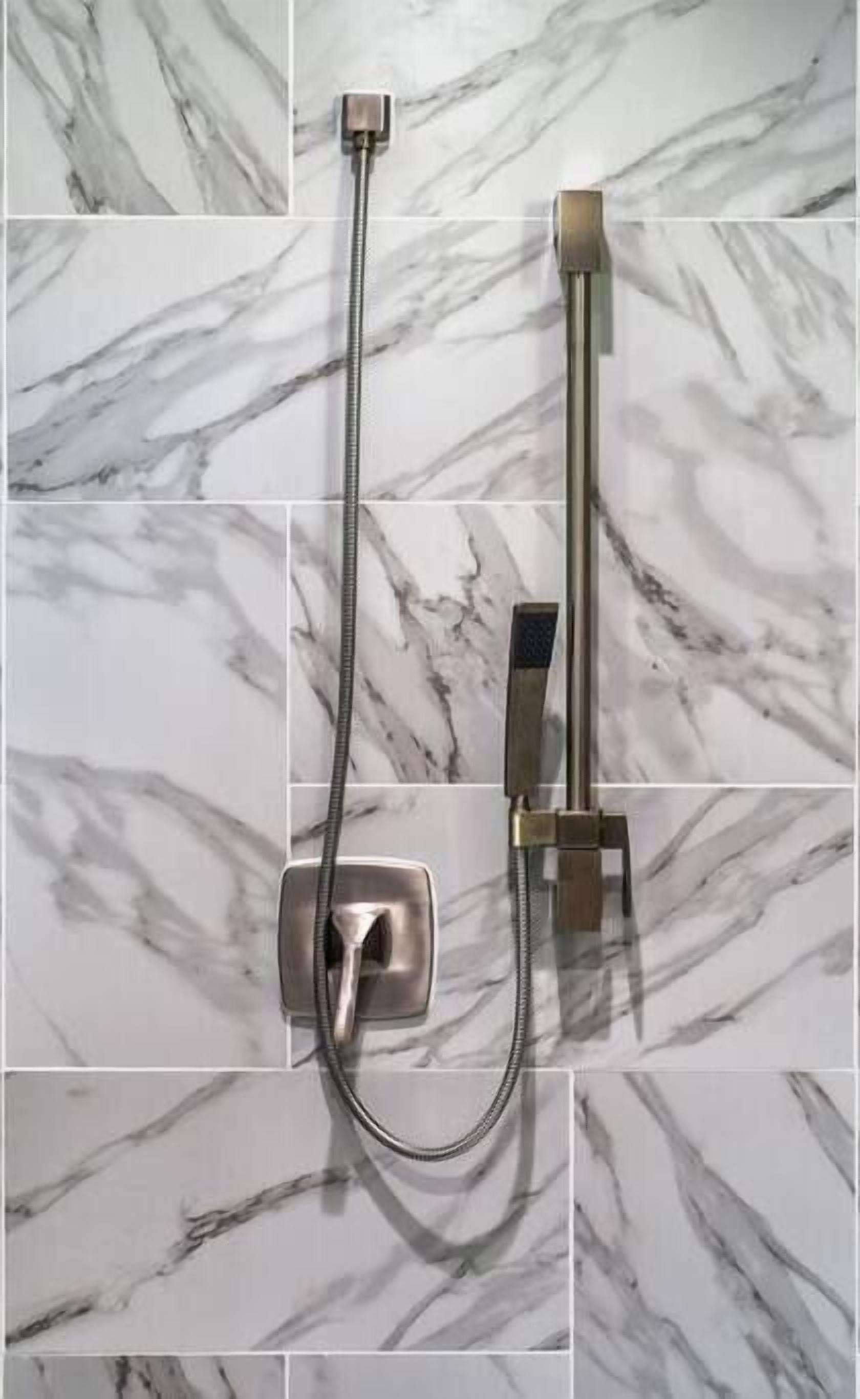 A shower with a handheld attachment on a marble-tiled wall.