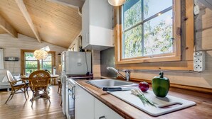 A kitchen with a wooden ceiling, a large window, a sink, and a dining area with wicker chairs. - Cozy home in Bogø By with WiFi (Bogø By)